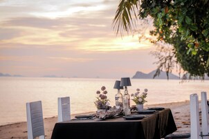 Una mesa preparada para una comida, con vista al mar y montañas al fondo.