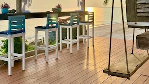 A wooden deck with a table and chairs, overlooking a beach at sunset. - Phangan Beach Resort (Ko Pha-ngan)