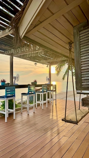 A wooden deck with a table and chairs, overlooking a beach at sunset. - Phangan Beach Resort (Ko Pha-ngan)