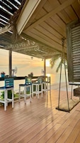 Una terraza de madera con una mesa y sillas, con vista a una playa al atardecer.