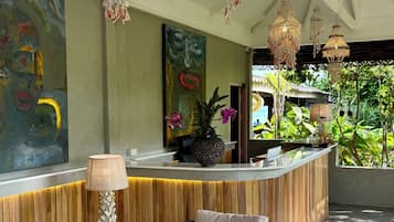 A modern reception area with a wooden reception desk, two cushioned chairs, a round table with a bowl of fruit, and a large abstract painting on the wall.