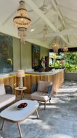 Un área de recepción moderna con un mostrador de madera, dos sillones acolchados, una mesa redonda con un frutero y un cuadro abstracto grande en la pared.