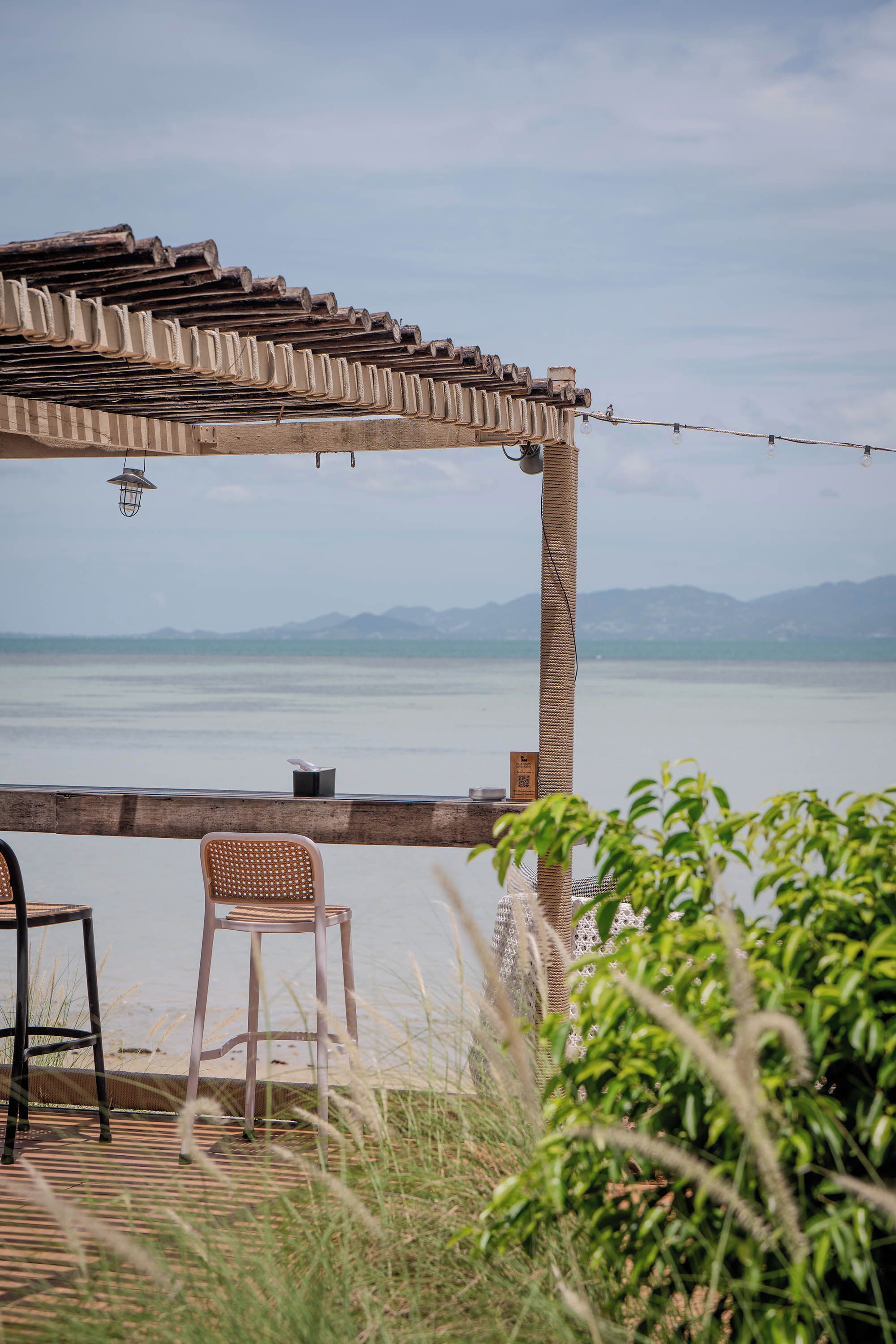A wooden deck with a pergola overlooking a body of water and distant mountains.
