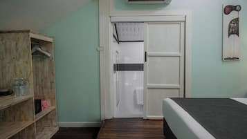 Una habitación con cama, un armario de madera, una puerta que da al baño y un equipo de aire acondicionado en la pared.