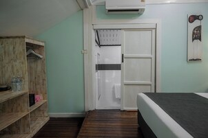Una habitación con cama, un armario de madera, una puerta que da al baño y un equipo de aire acondicionado en la pared.