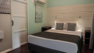 Une chambre à coucher comprenant un lit, une table de chevet, un climatiseur fixé au mur, une porte et un tableau.