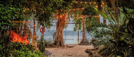 A pathway leading to a beach with string lights and tropical vegetation.