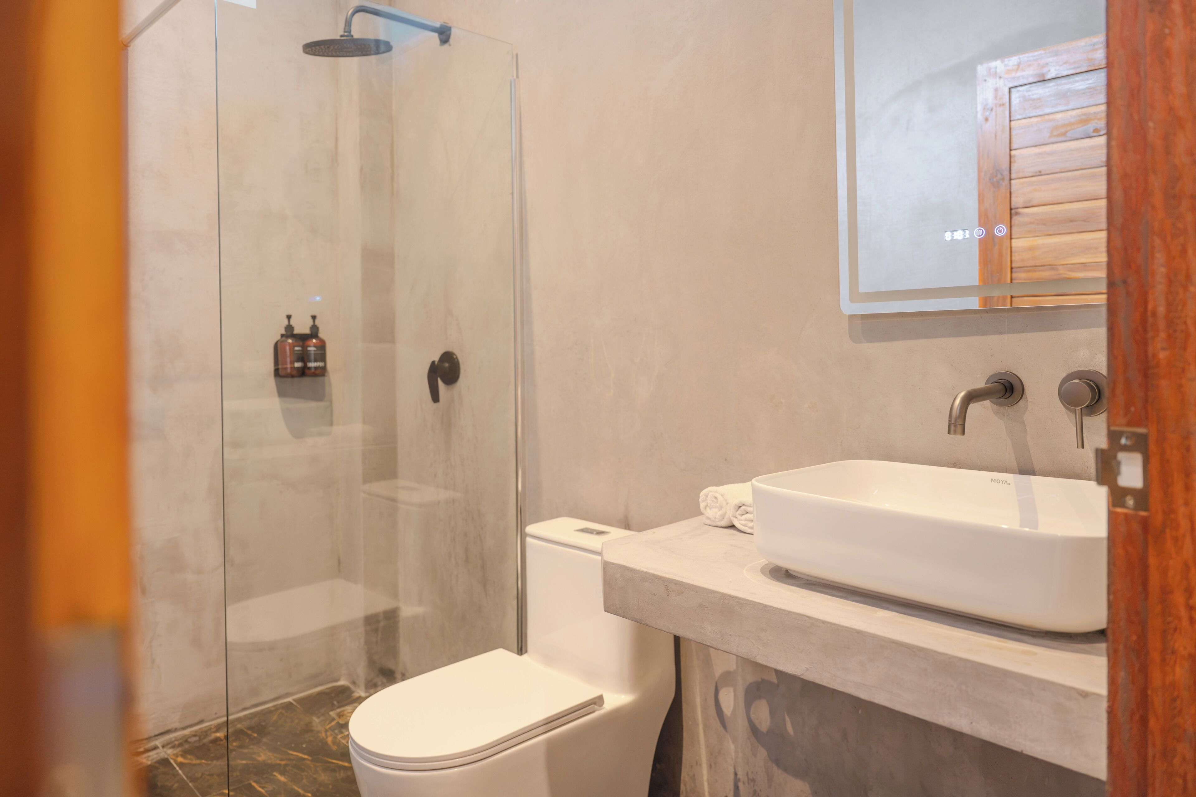 Un baño moderno con ducha de vidrio, inodoro y lavabo con espejo.
