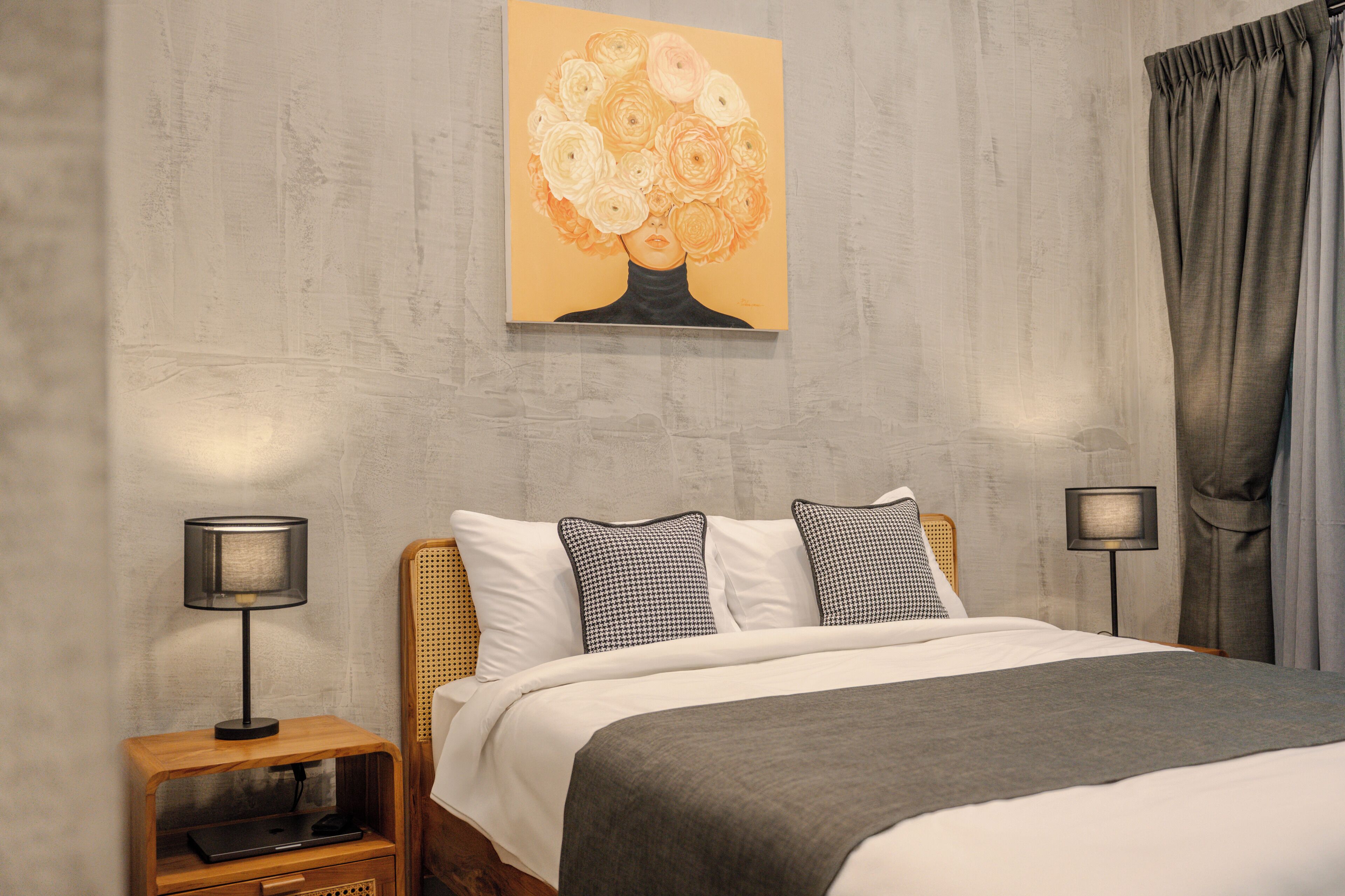 A bedroom with a bed, two bedside tables, a lamp, a painting, and a curtain.