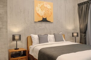 Un dormitorio con una cama, dos mesitas de noche, una lámpara, un cuadro y una cortina.