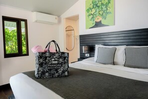 A hotel room with a bed, a large black and white patterned bag, a window with a view of trees, and a painting of a tree on the wall. - Phangan Beach Resort (Ko Pha-ngan)