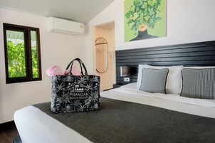 Una habitación de hotel con una cama, un bolso grande blanco y negro estampado, una ventana con vista a árboles y un cuadro de un árbol en la pared.