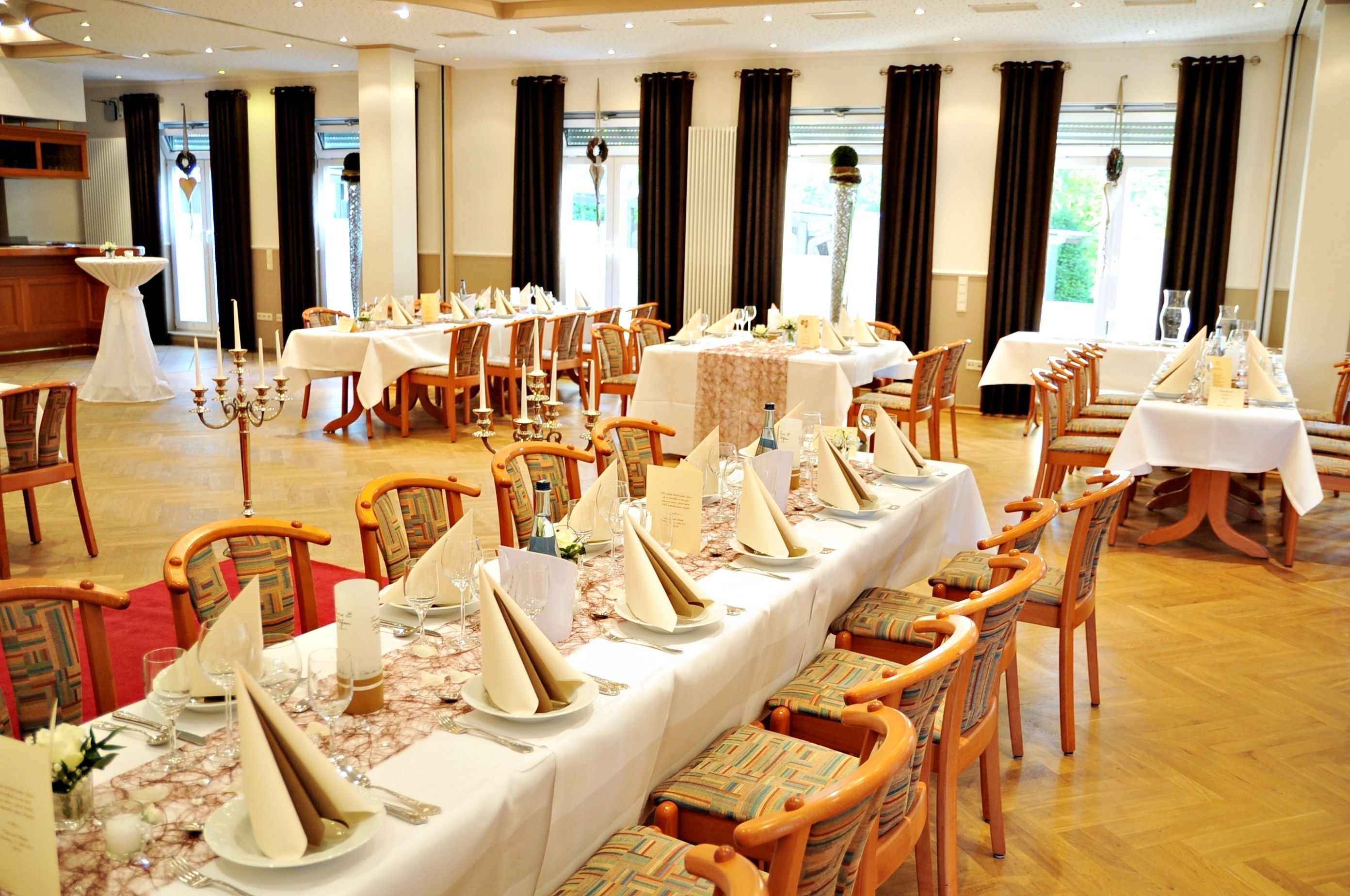 A banquet hall with multiple round tables set for dining, wooden chairs, and a chandelier.