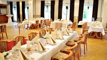 A banquet hall with multiple round tables set for dining, wooden chairs, and a chandelier.