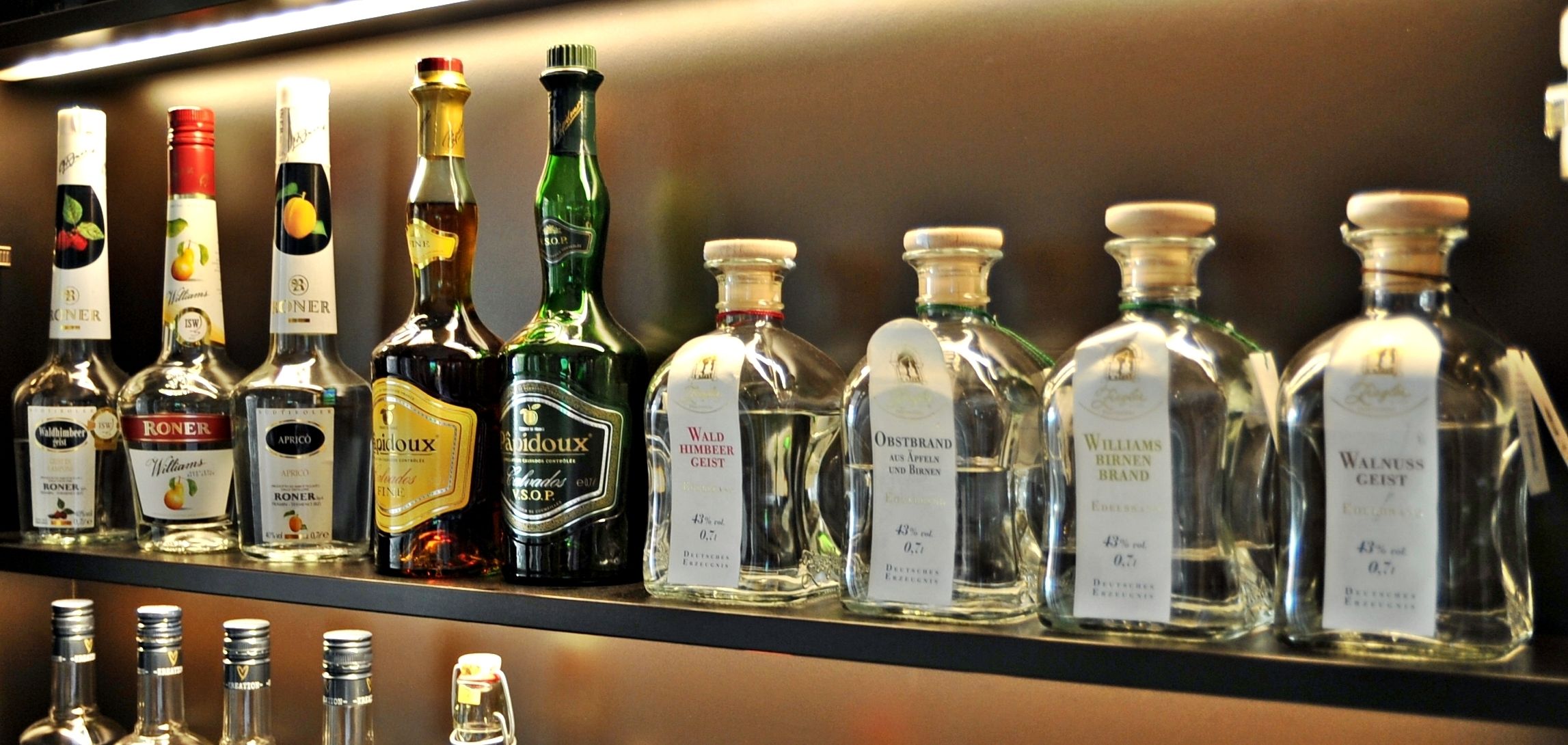 A shelf with various bottles of alcohol, including brands like RONER, Williams, and Wald Himmer.