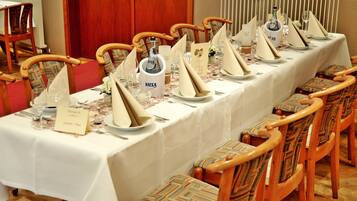 A long dining table set for a formal meal with multiple chairs, a white tablecloth, and V.I.S.A. branded champagne.