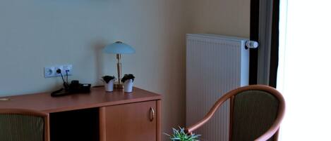 A hotel room with a bed, a desk, a chair, a TV, and a radiator.
