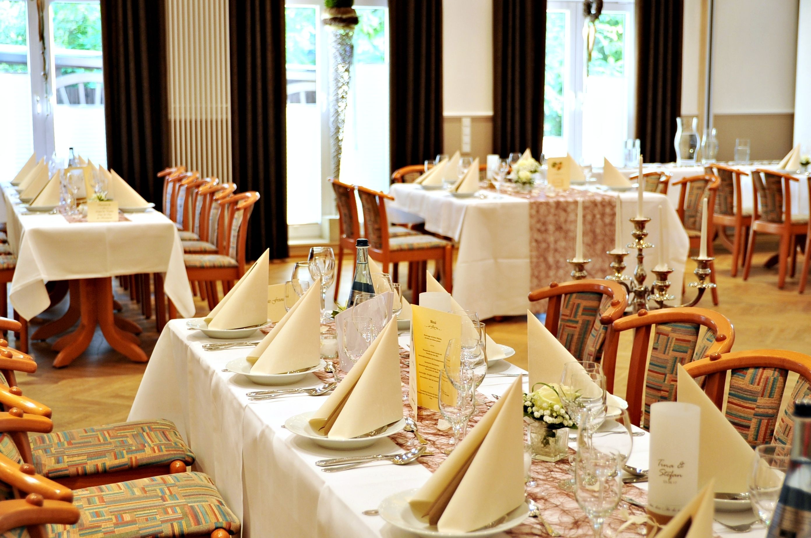 Un comedor formal con varias mesas dispuestas para el servicio, cada una con manteles blancos, servilletas dobladas con esmero y cristalería.