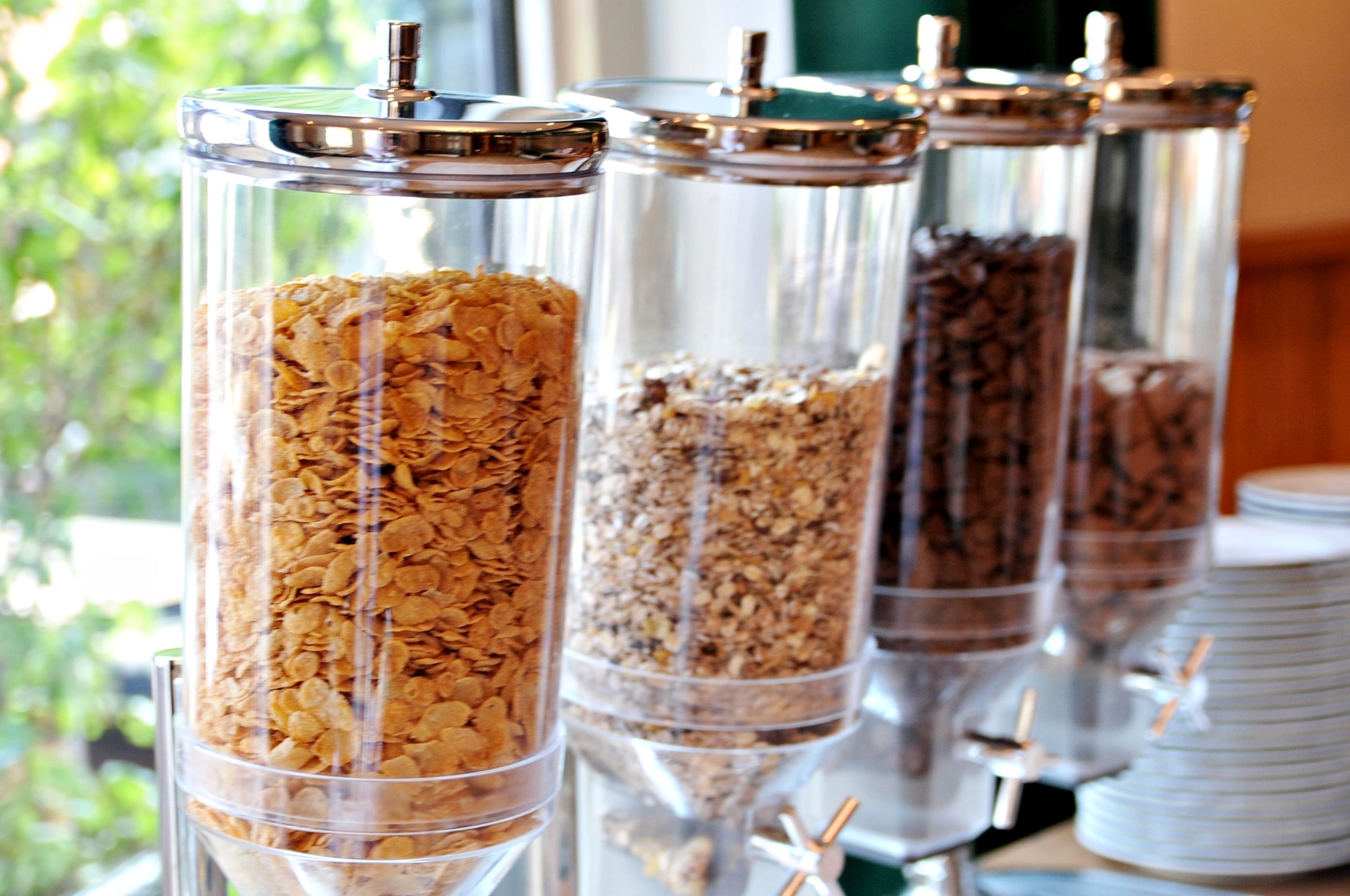Quatro dosadores de vidro com tampas de metal, cada um com tipos diferentes de granola.