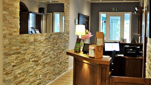 A reception area with a stone wall, wooden reception desk, and a computer monitor. - Hotel Restaurant Burgerklause Tapken (Garrel)