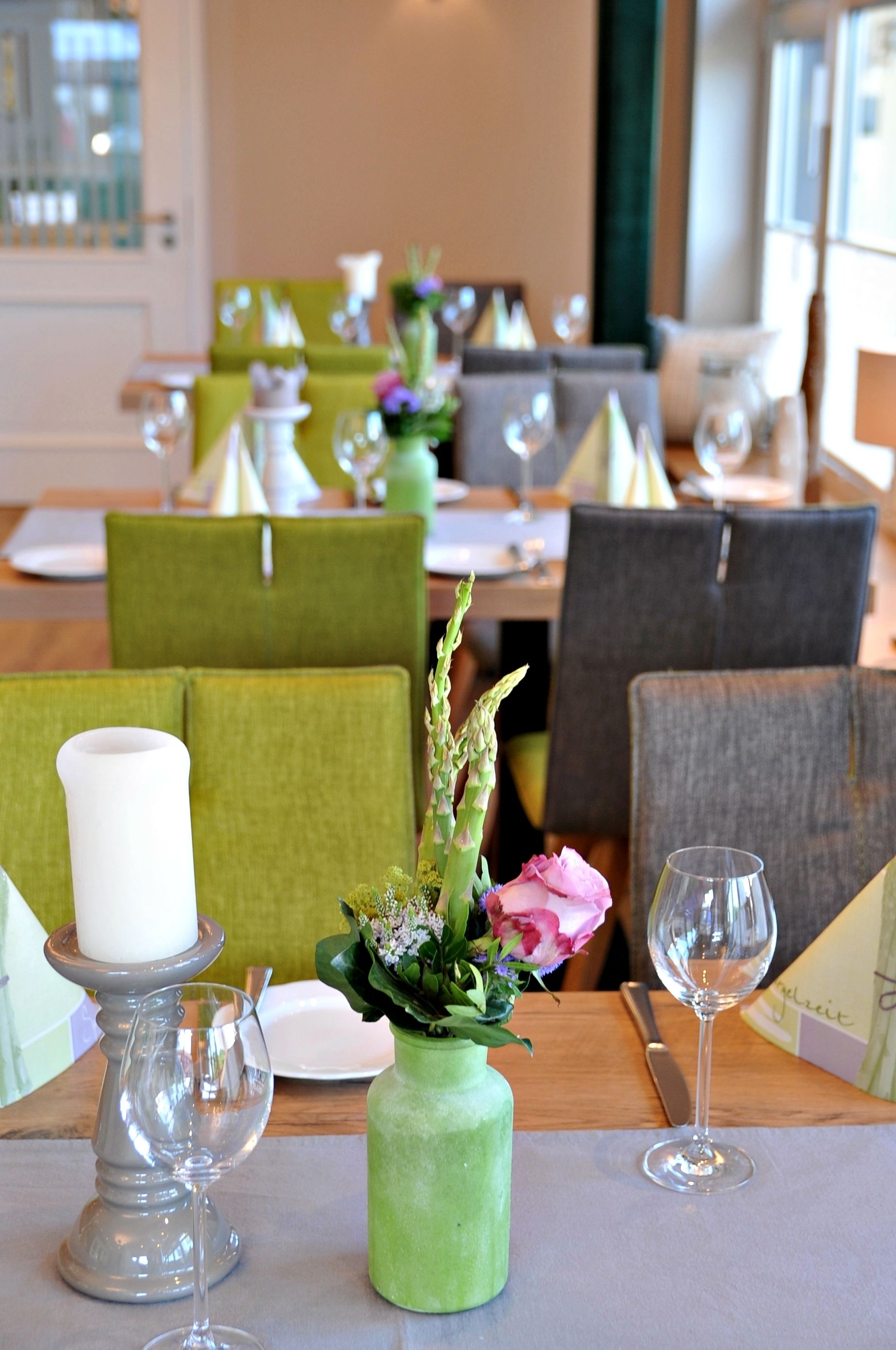 A dining area with green upholstered chairs, a table set with plates, glasses, and a vase with flowers.