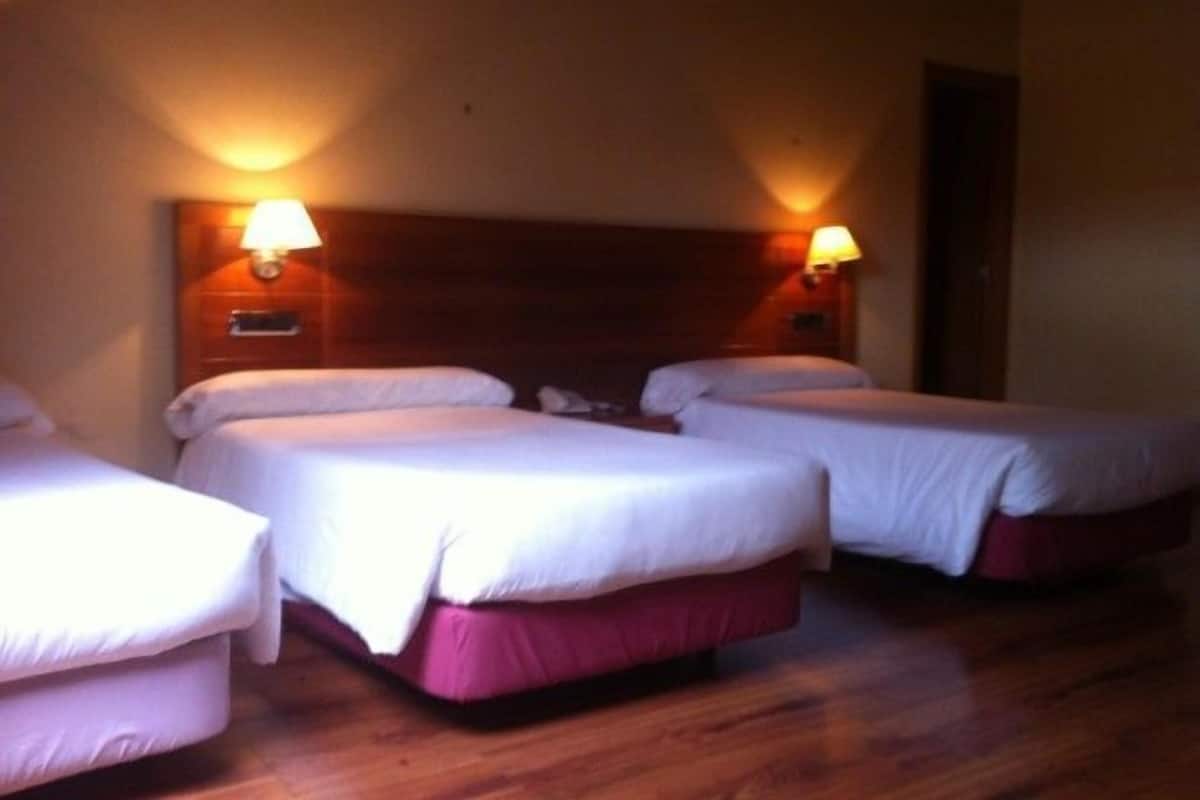 A hotel room with two single beds, wooden headboards, and wall-mounted lamps.