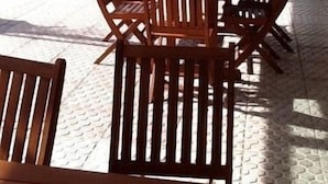 Un espace extérieur aménagé avec des tables et des chaises en bois, une entrée couverte et une vue sur la rue et les bâtiments en arrière-plan.