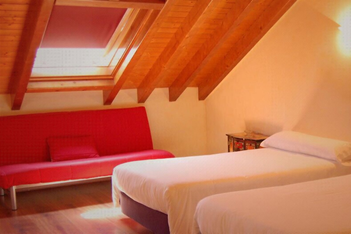 A room with two beds, a red sofa, a skylight, and a wall-mounted light fixture.