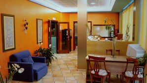 Un hall d’hôtel avec un canapé bleu, un comptoir d’accueil en bois et un sol carrelé.