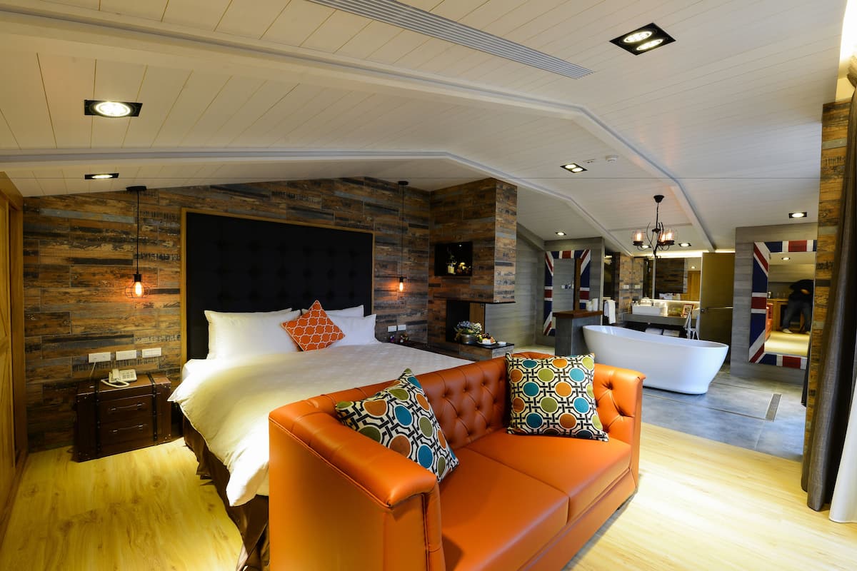 A modern bedroom with a large bed, an orange sofa, a bathtub, and a wooden accent wall.