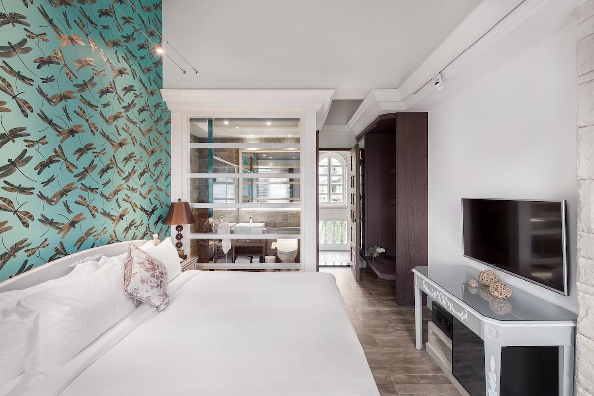 A bedroom with a bed, a TV, and a bathroom visible through a glass door.