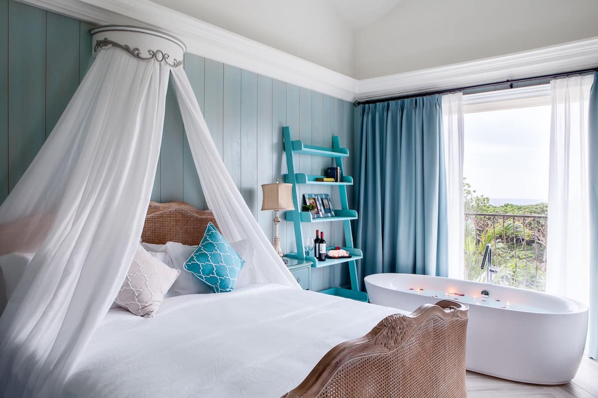 A bedroom with a canopy bed, a bathtub, and a view of the outdoors.