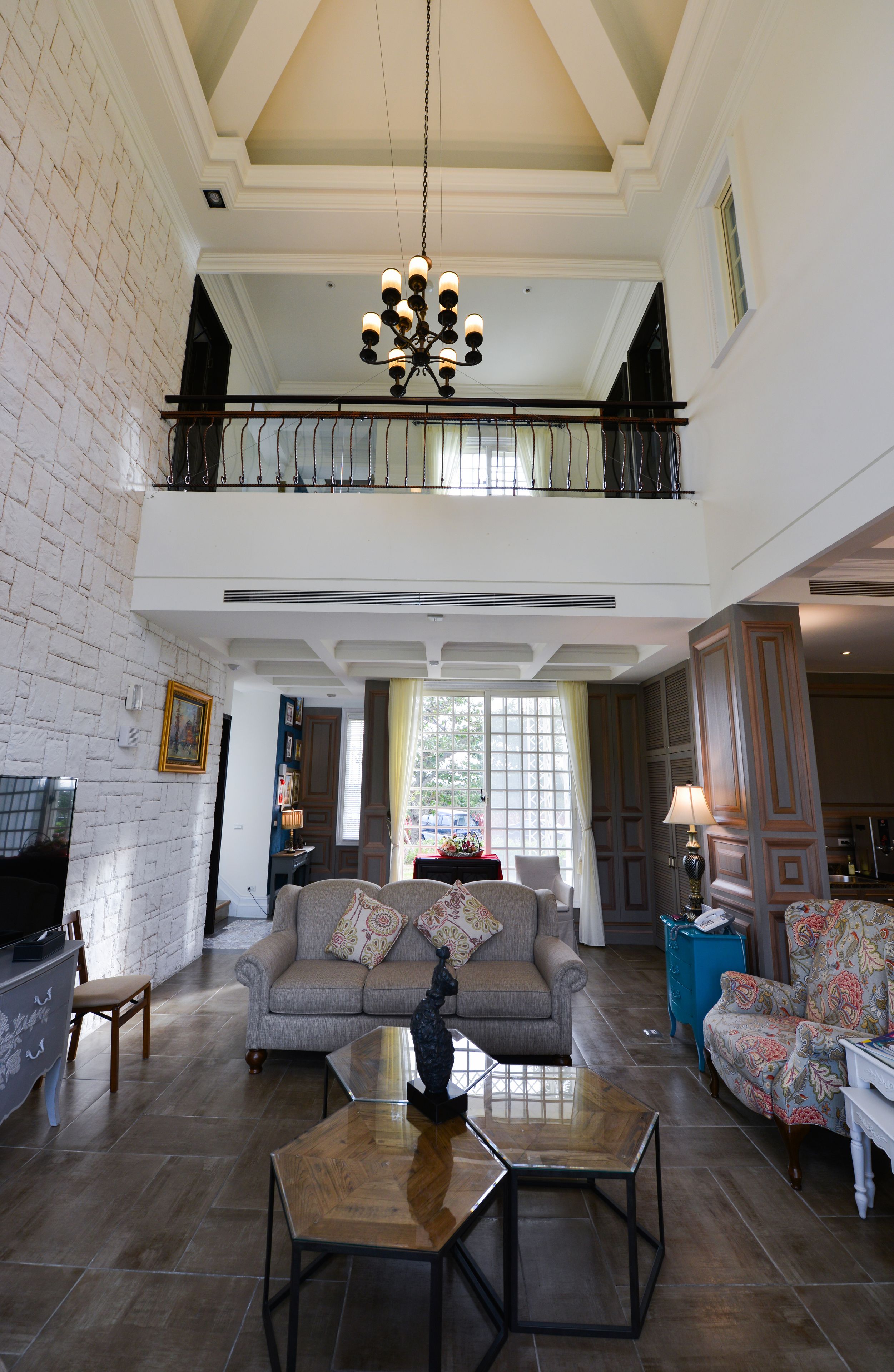 A spacious living room with a high ceiling, a chandelier, a sofa set, and a television.