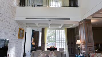 A spacious living room with a high ceiling, a chandelier, a sofa set, and a television.