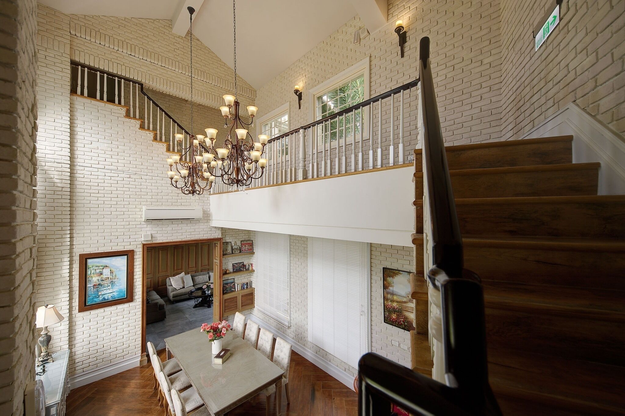 Un interior espacioso con techo alto, una escalera con barandilla de madera y un candelabro.