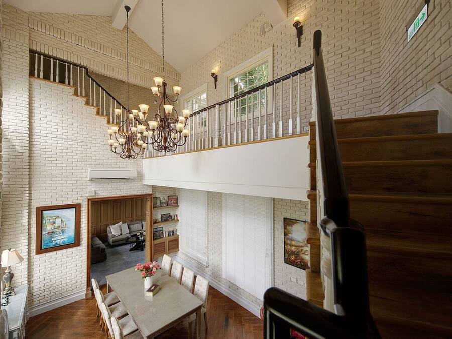 Un interior espacioso con techo alto, una escalera con barandilla de madera y un candelabro.