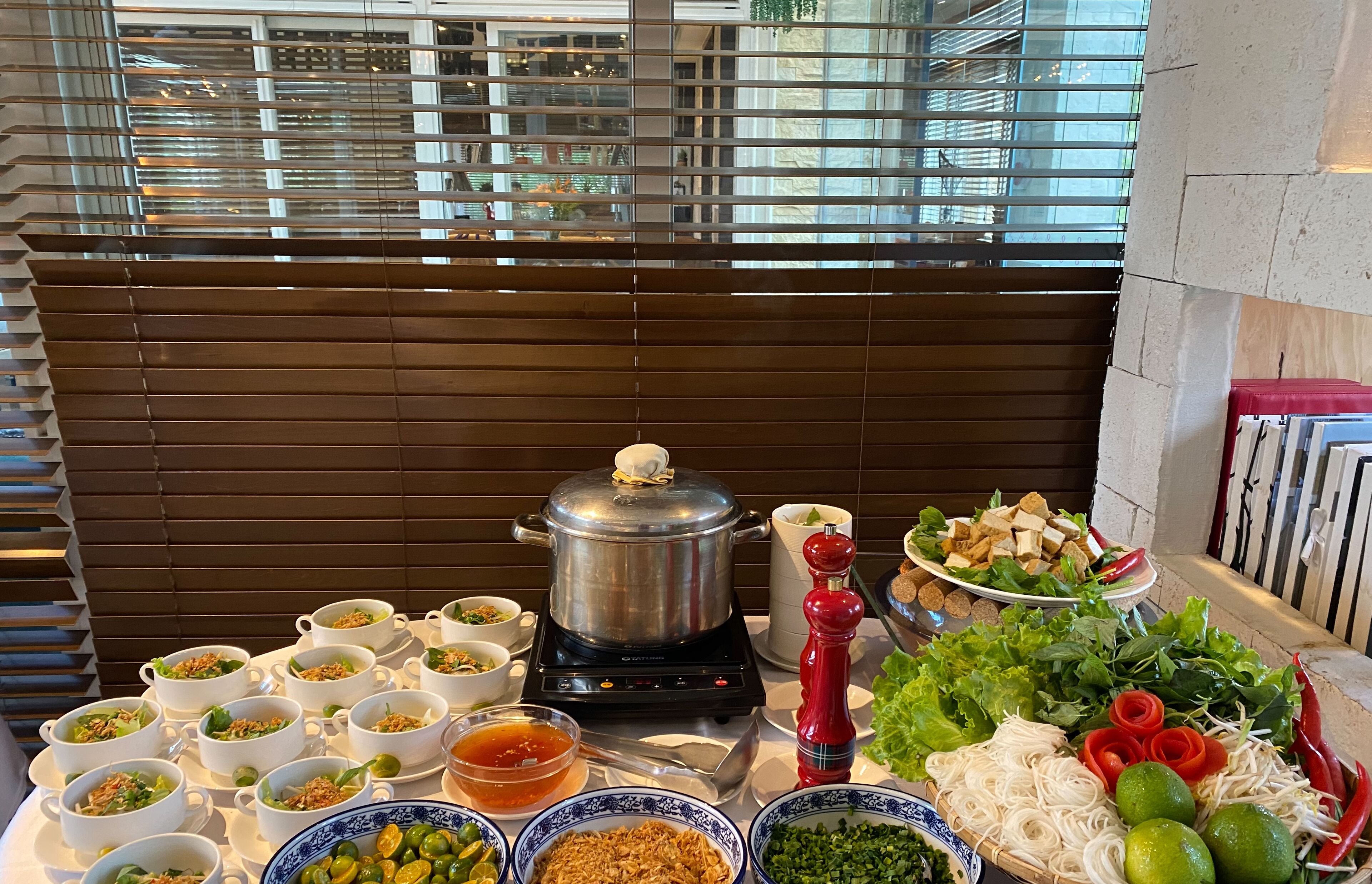 Une table de buffet garnie de différents plats, une grande marmite sur une cuisinière et des légumes frais.