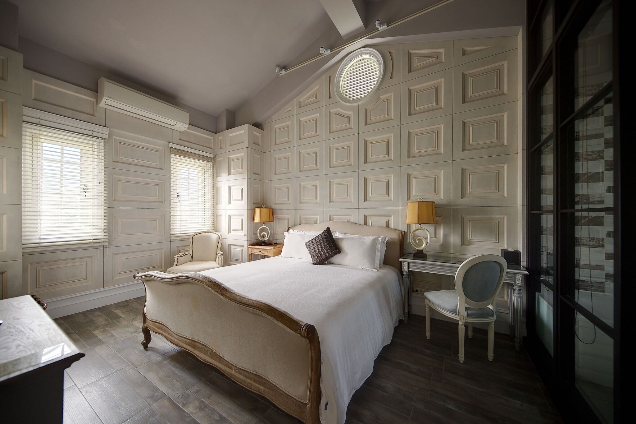 A bedroom with a large bed, two bedside tables with lamps, a chair, and a desk.