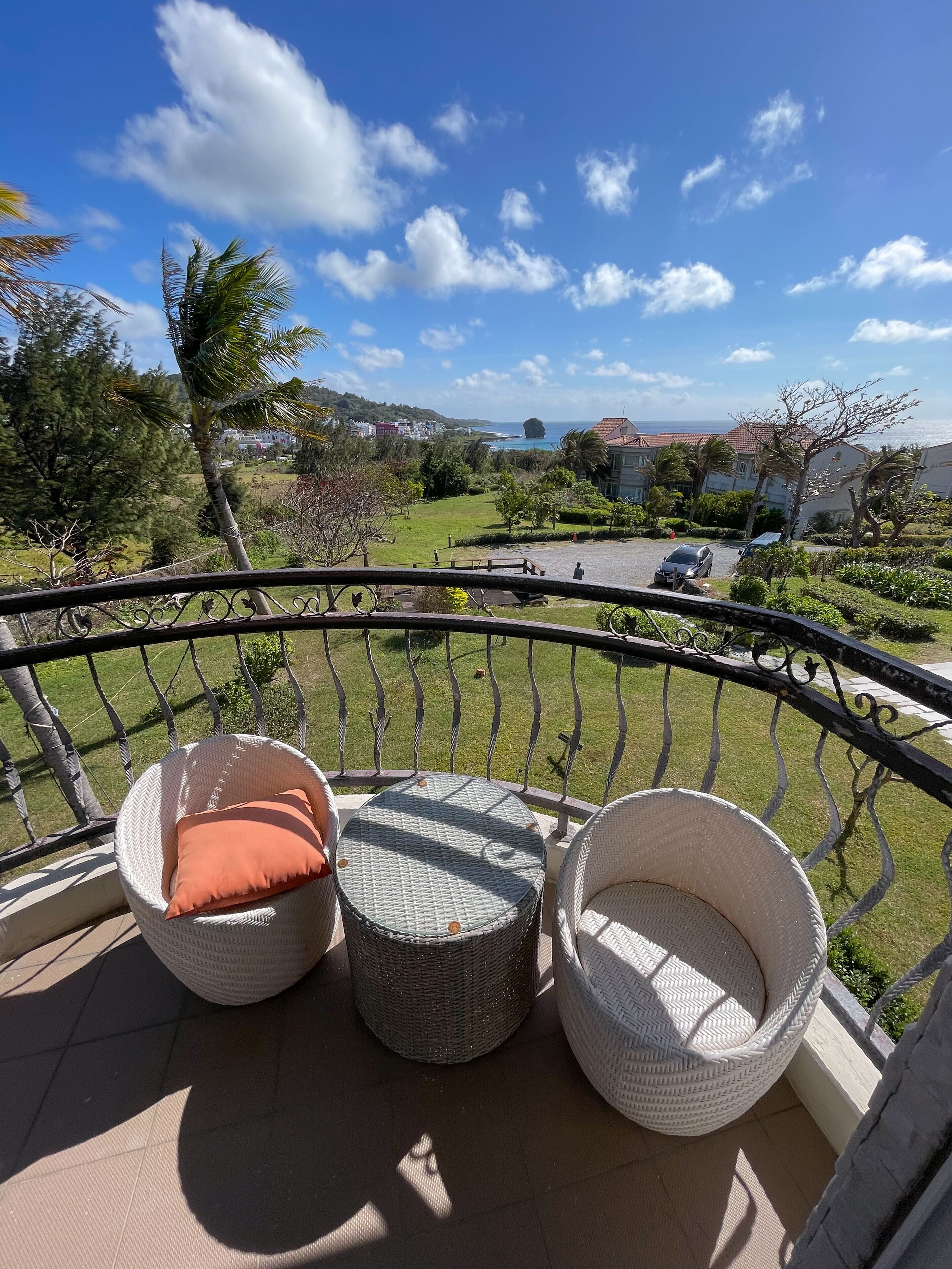 A balcony with wicker furniture, a view of the sea, and a grassy area with trees.