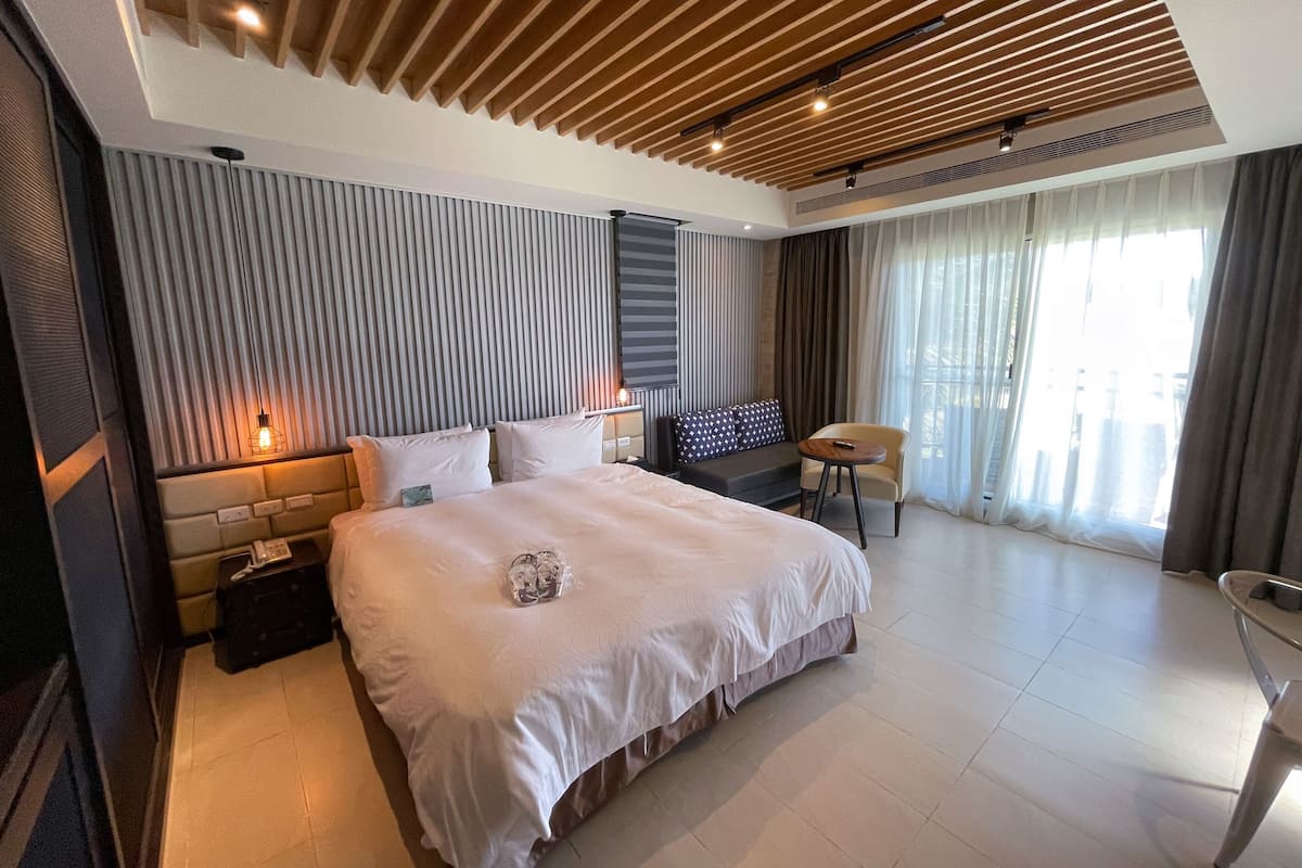A modern hotel room with a large bed, a sofa, a chair, and a TV.