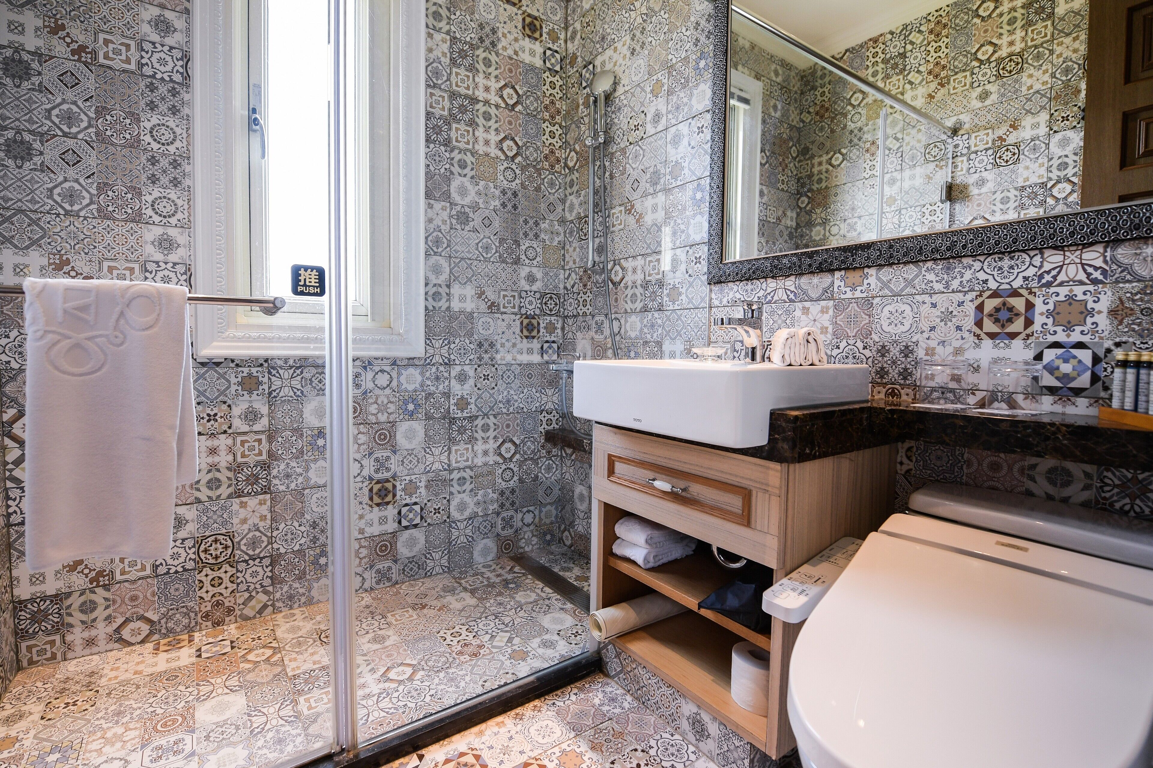 Un baño con baldosas estampadas, cabina de ducha de cristal, lavabo e inodoro.