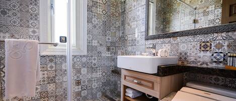A bathroom with patterned tiles, a glass shower enclosure, a sink, and a toilet.