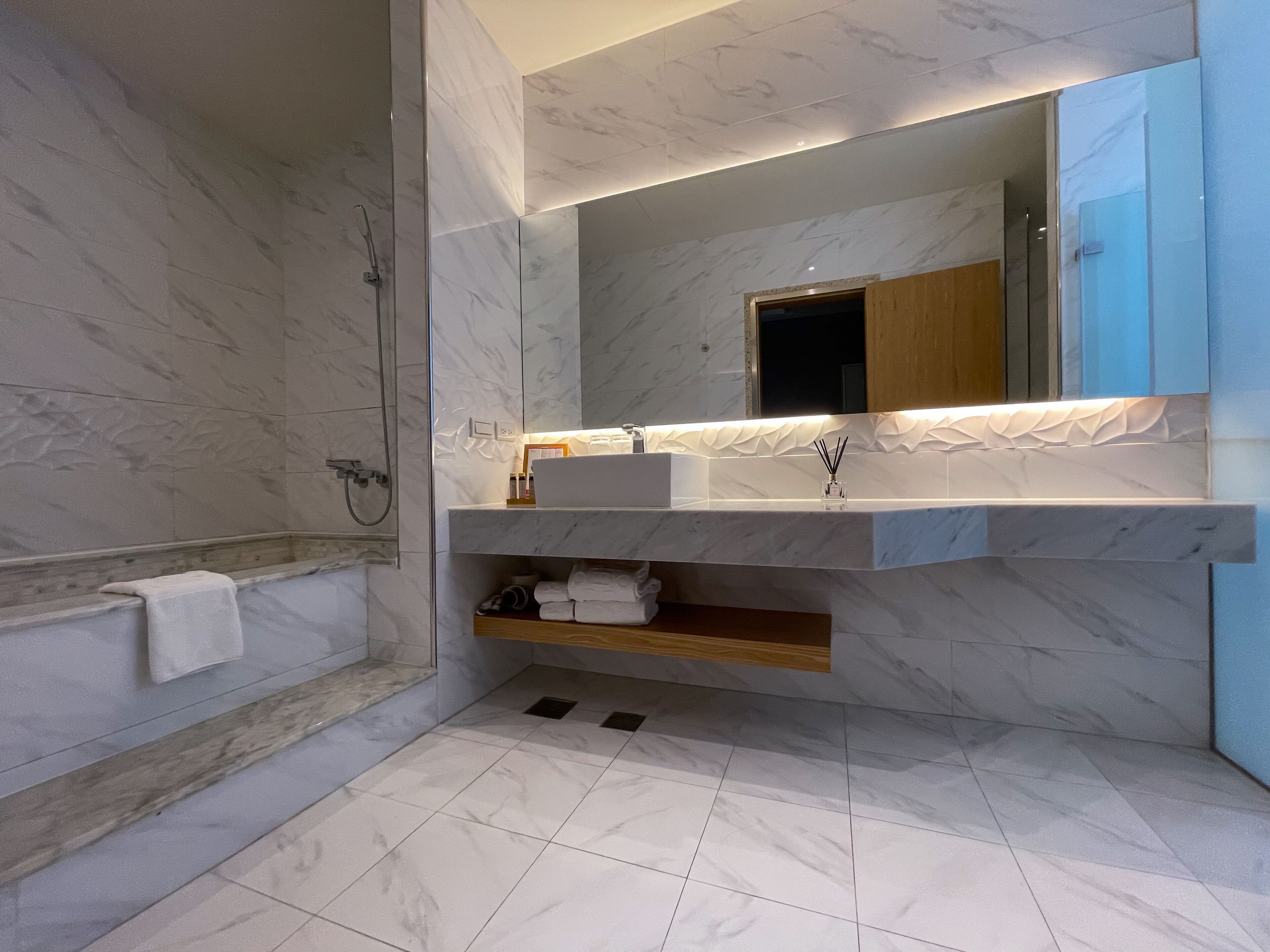 A modern bathroom with a marble sink, a large mirror, and a shower.