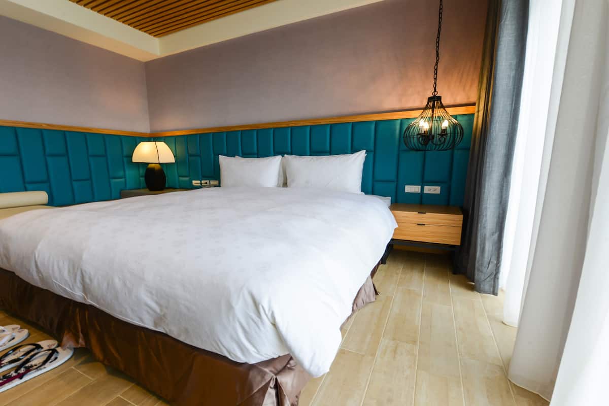 A neatly made bed in a hotel room with a headboard, a bedside table with a lamp, and a hanging light fixture.
