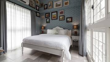 A bedroom with a white bed, grey curtains, and a brick-patterned wall with framed pictures.