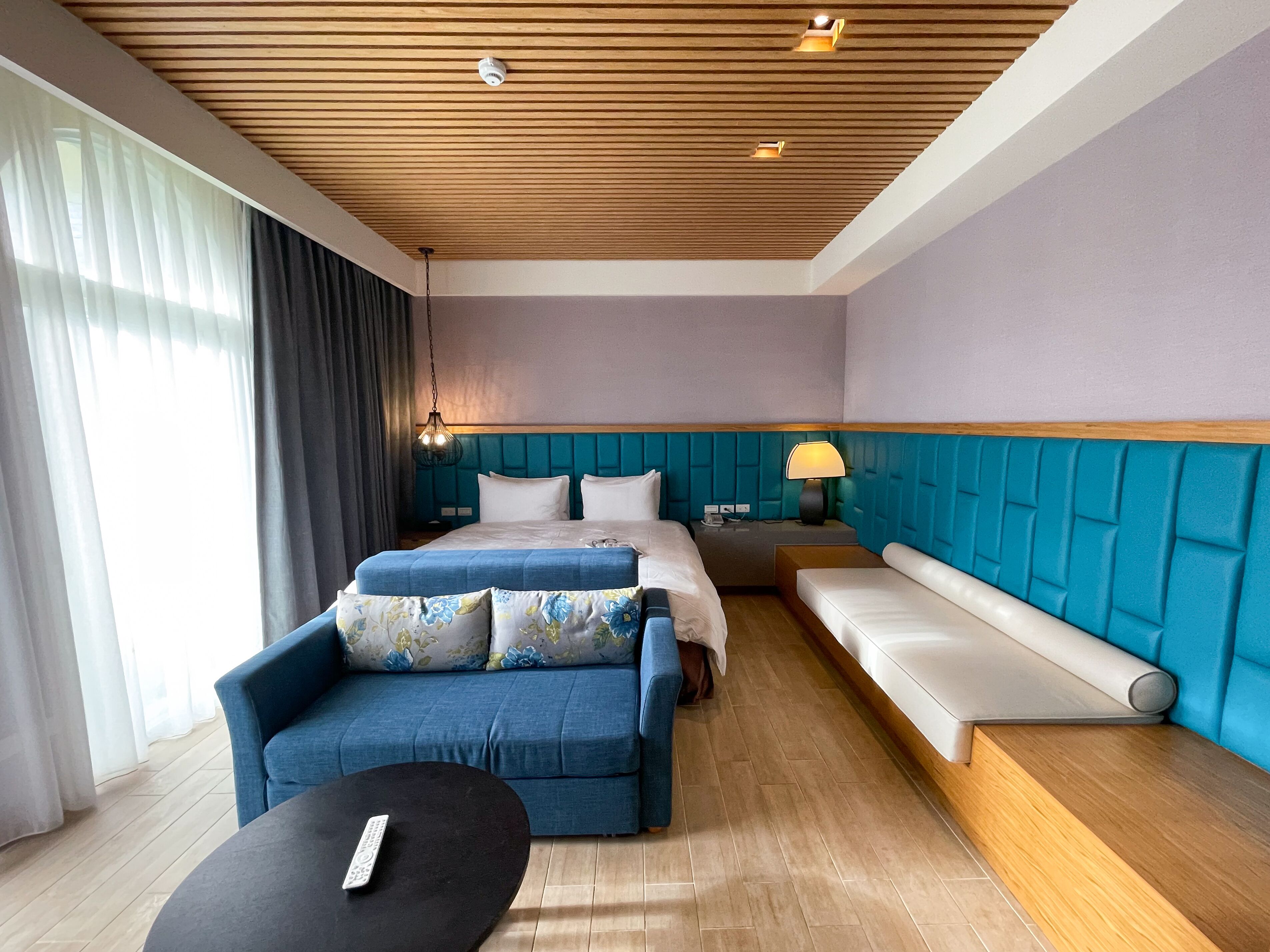 A hotel room with a bed, a sofa, a small table, and a nightstand with a lamp.