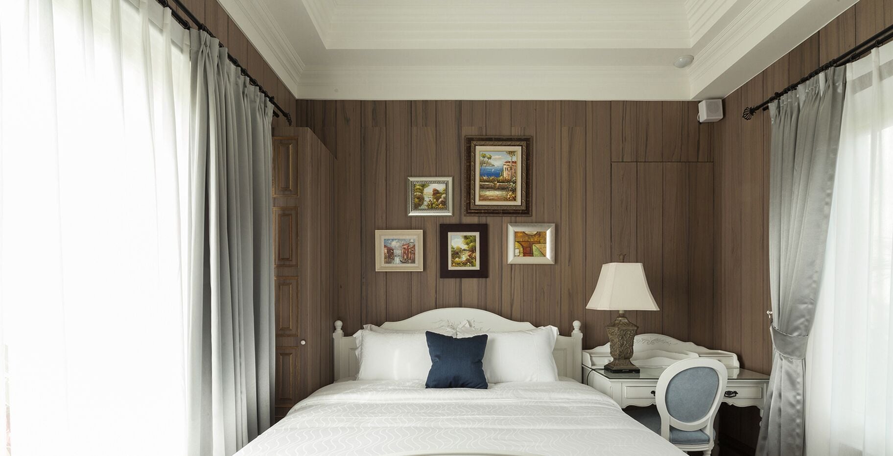 Habitación de hotel con una cama grande, un escritorio con lámpara y cuatro cuadros en la pared.