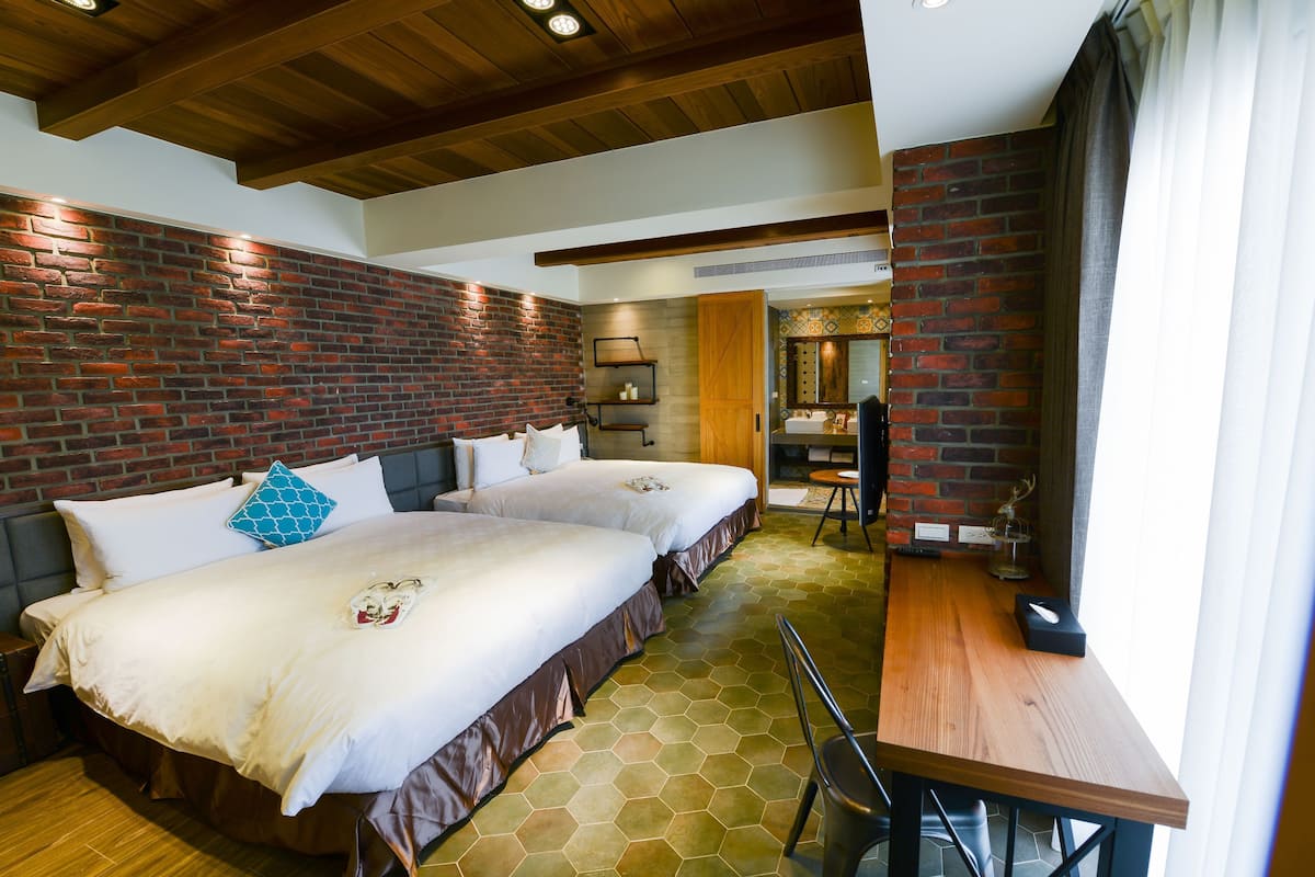 A hotel room with two beds, a wooden table, and a brick wall.