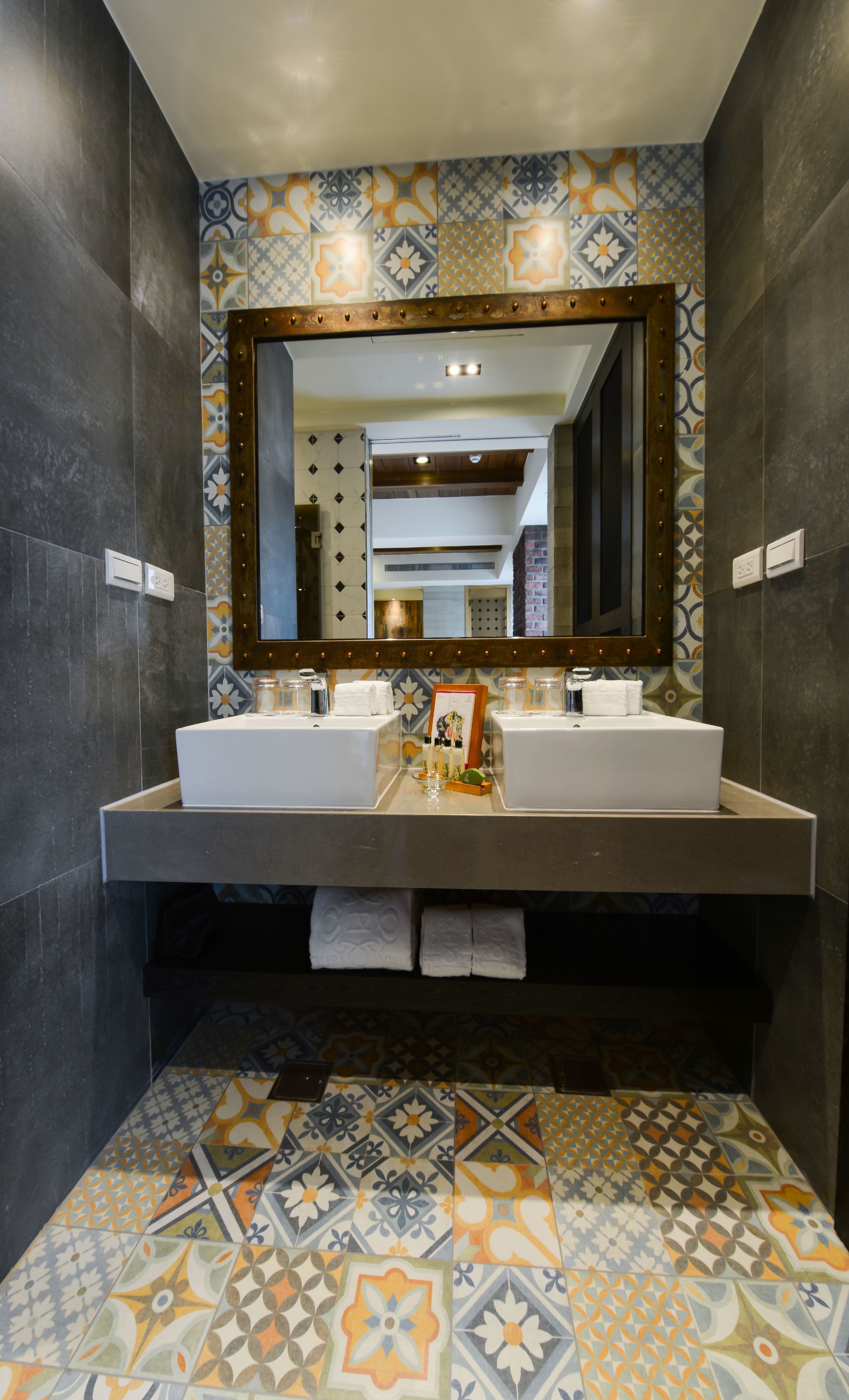 A bathroom with two sinks, a mirror, and patterned tiles on the floor and walls.