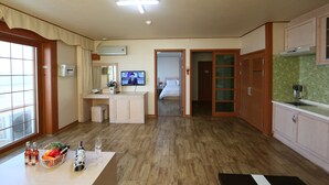 A hotel room with a wooden floor, a kitchenette, a dining area, a bathroom, and a TV.